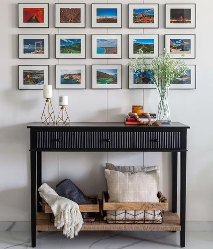 Black fluted console table beneath a gallery wall of framed travel photographs in a foyer