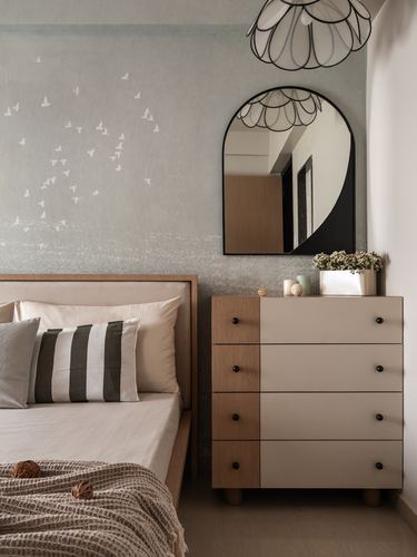 Bedroom corner with arched mirror over a two-tone dresser beside a bed with striped pillows