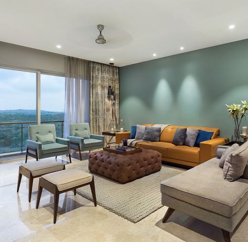 Living room with sage wall, mustard sofa, tufted ottoman, and balcony view over greenery