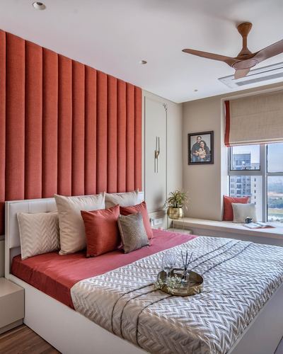 Bedroom with coral fluted fabric headboard wall, wooden ceiling fan, and window seat overlooking city