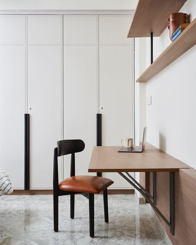 Wall-mounted wooden desk with black chair beside white wardrobes and floating shelves