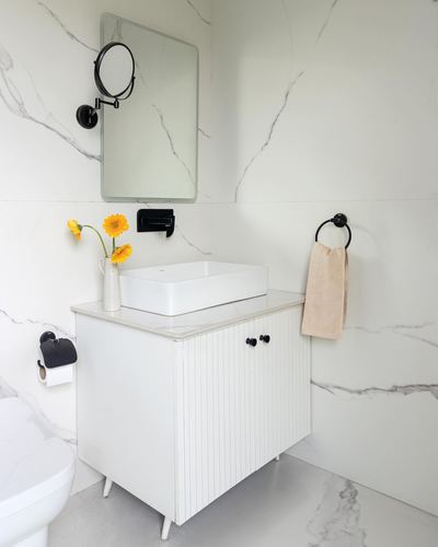 White bathroom vanity with vessel sink, fluted cabinet, mirror and marble-look walls