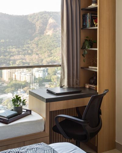 Wooden study nook with desk, chair and shelves overlooking Mumbai hills through glass balcony railing