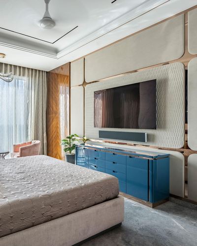 Bedroom with padded geometric wall, mounted tv, and glossy blue console below.