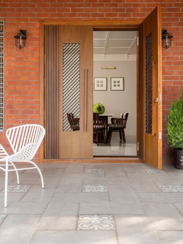 Wooden front door with diagonal fluting set in exposed brick facade, open to dining room beyond