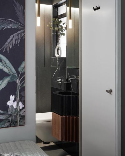 Doorway view into a dark marble-clad powder room with fluted wood vanity and pendant lights