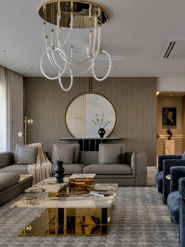 Living room with grey sofas, marble coffee table, round mirror, and looping chandelier over patterned rug