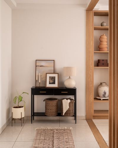 Entryway with black console table, framed art, lamp, rattan baskets, and adjacent wooden display shelves