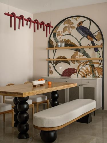 Dining table with bulbous black legs beneath an arched bird-and-ginkgo mural wall unit