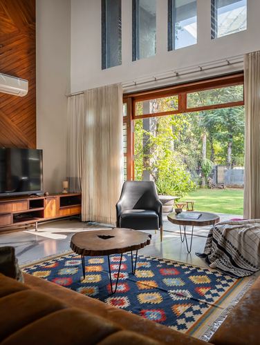 Double-height living room with kilim rug, live-edge tables, and glass wall opening to garden