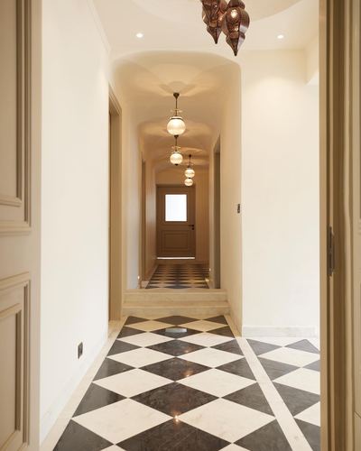 Corridor with black-and-white diamond marble floor and vaulted ceiling leading to a glass-paned door