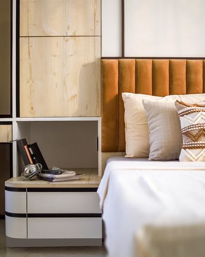 Bedroom corner with fluted tan velvet headboard, light wood cabinetry, and open nightstand with books