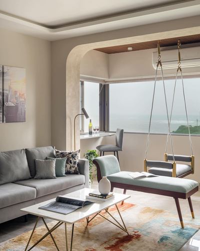 Living room with grey sofa, marble-top coffee table and hanging swing chair facing sea view