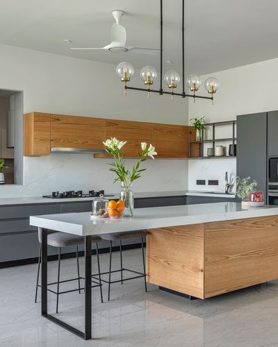 Modern kitchen with wood cabinetry, grey lower units, marble-look island and globe pendant lights