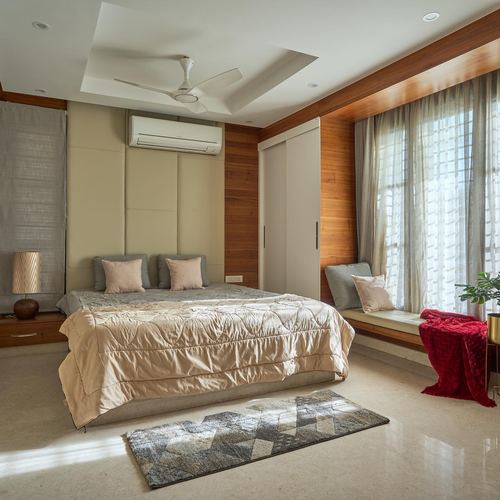 Bedroom with wood-paneled walls, upholstered headboard, window seat, and beige stone flooring