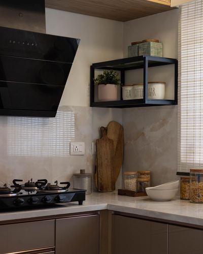Corner kitchen with black chimney hood, floating black shelf with jars, marble backsplash and countertop.