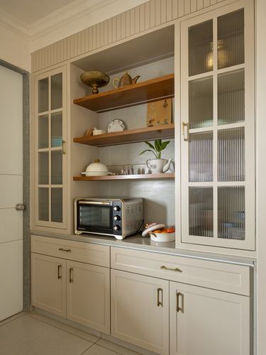 Cream kitchen cabinetry with reeded glass doors and open wood shelves displaying crockery and a toaster oven