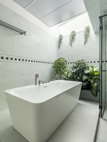White freestanding bathtub under skylight with hanging plants in marble-clad bathroom