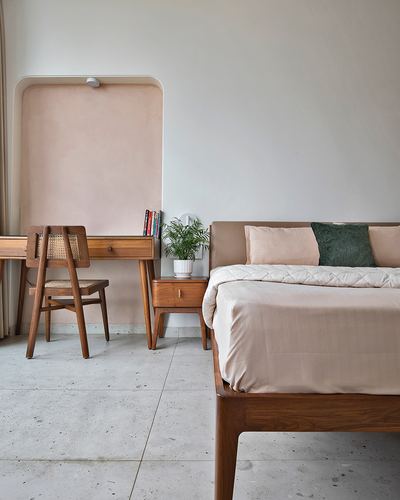 Bedroom with wooden bed, cane chair, and arched niche desk against pink wall