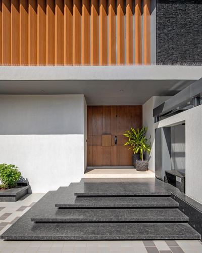 Entrance facade with wooden pivot door, cantilevered stone steps, and vertical wood fins above