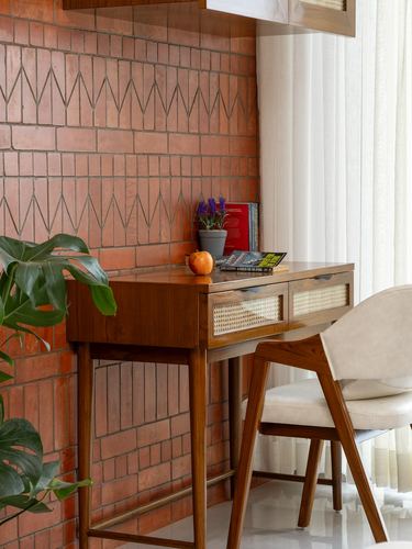 Wooden desk with cane drawers against a chevron-patterned brick wall in a Nashik home