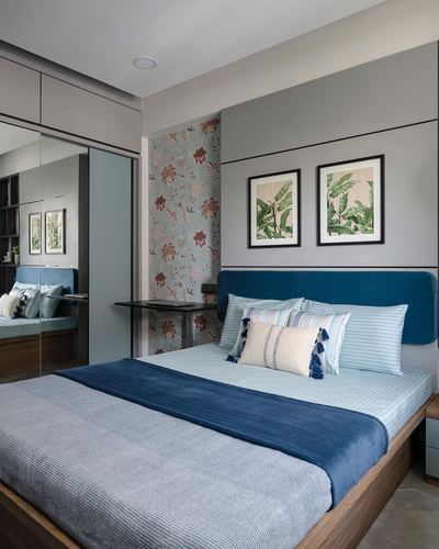 Bedroom with blue velvet headboard, floral wallpaper accent, and botanical prints above a bed.