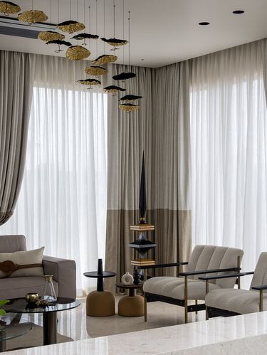 Living room with tall sheer curtains, boucle armchairs and sculptural gold pendant lights