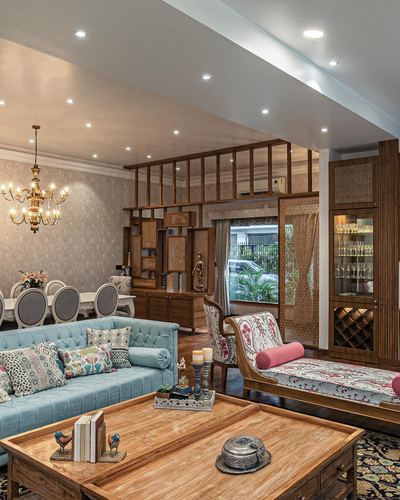 Living room with blue tufted sofa, wooden coffee table, patterned daybed and carved wood partition to dining area