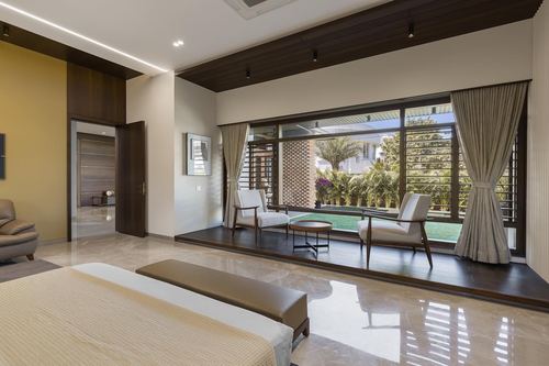 Bedroom with marble floor opening to a sunken wood-floored sitting alcove facing garden windows