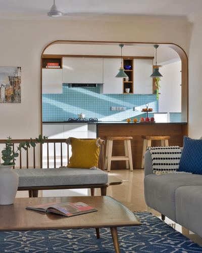 Living room with arched wooden opening to teal-tiled kitchen, blue rug and grey sofa