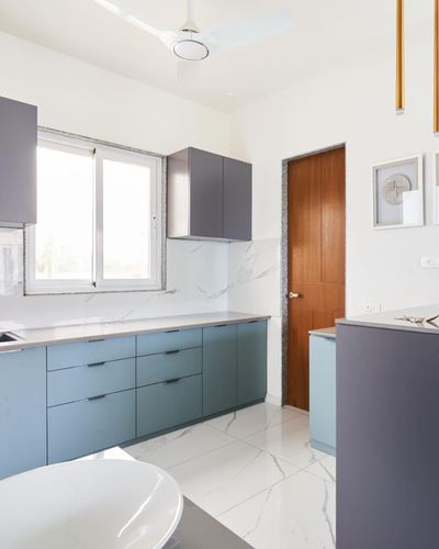 Modern kitchen with fluted blue cabinets, stone counters, marble-look floor and backsplash, wooden door