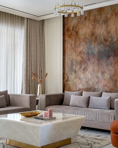 Living room with taupe velvet sofas around a marble coffee table beneath a large veined stone wall panel