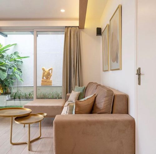 Beige velvet corner sofa beside glass door opening to a small courtyard with plants
