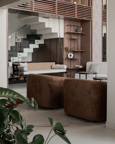 Living room with brown velvet armchairs, cane swing bench, and open staircase beyond