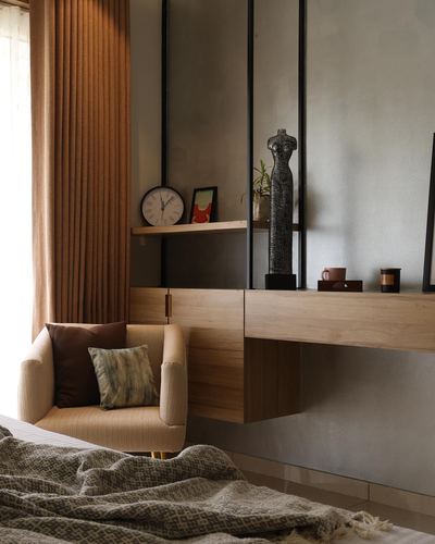 Bedroom corner with floating wood cabinet, glass partition shelf, sculpture, and tan armchair