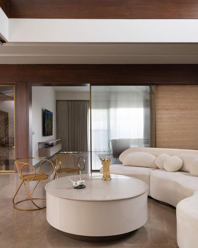 Curved cream sofa and round marble-top table beside cane chairs, with a wood-panelled beam ceiling and glass divider to another room.