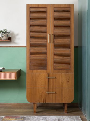 Tall teak louvre-door cabinet with brass handles against a sage green and white wall