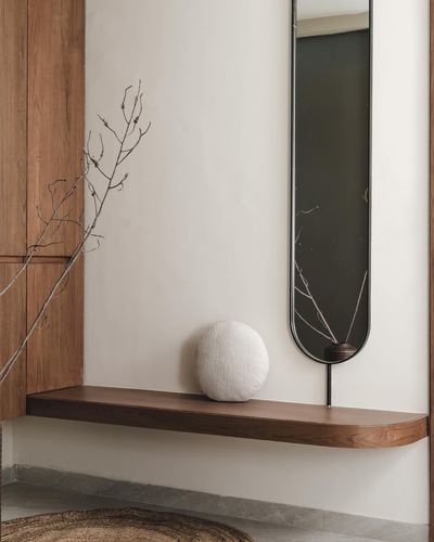 Floating walnut shelf below an elongated capsule mirror with dried branches and a round cushion