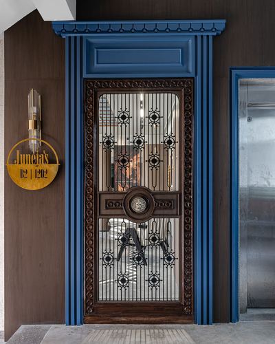 Ornate wood and iron entrance door with blue pedimented surround and brass sconce