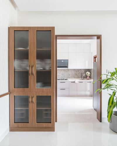 Fluted-glass wooden crockery cabinet beside a doorway opening into a white modular kitchen