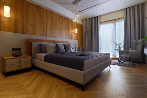 Bedroom with wood-panelled wall, upholstered bed, herringbone floor and sheer-curtained window
