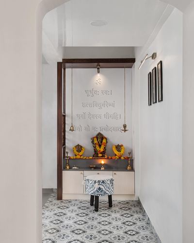 Pooja niche at end of white corridor with Ganesha idol, marigold garlands, and patterned floor tiles