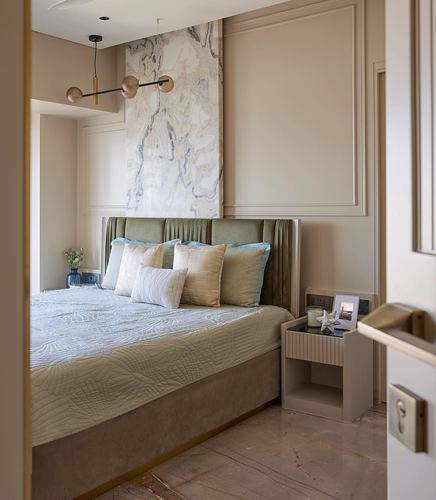 Bedroom with green velvet headboard, marble accent wall, and pastel pillows viewed through open doorway