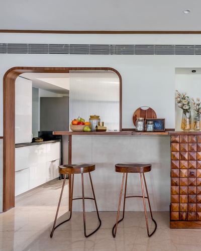 Arched wooden frame opens to a white kitchen with a stone bar counter and two wooden stools