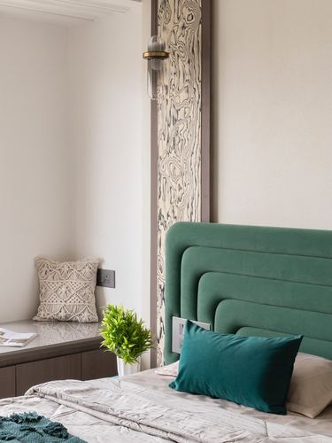 Bedroom corner with green channel-tufted headboard, teal cushion, and patterned veneer wall strip