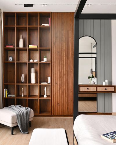 Wooden grid shelving beside a ribbed wood panel, with an arched mirror and cane console visible through a black bed frame.