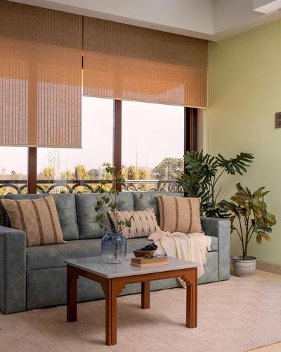 Sage-green living room with grey sofa, wooden coffee table, and bamboo blinds facing a balcony