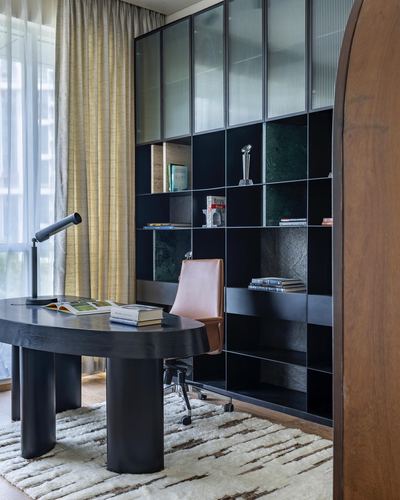 Dark oval desk with leather chair before a black shelving unit with glass and stone panels