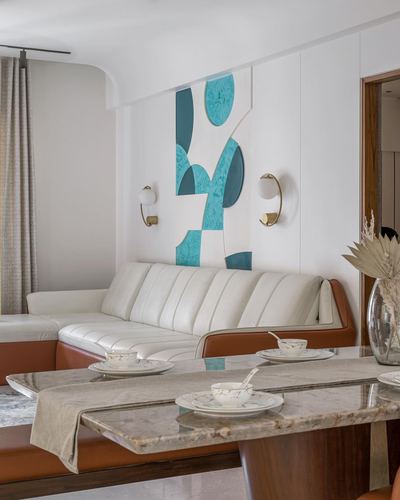 Dining table with marble top in front of a cream sofa and teal wall art panel