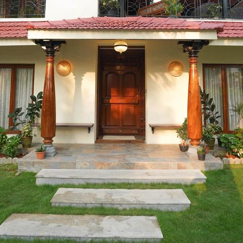 Villa entrance porch with carved wooden door, turned wood columns, and stone steps leading through lawn